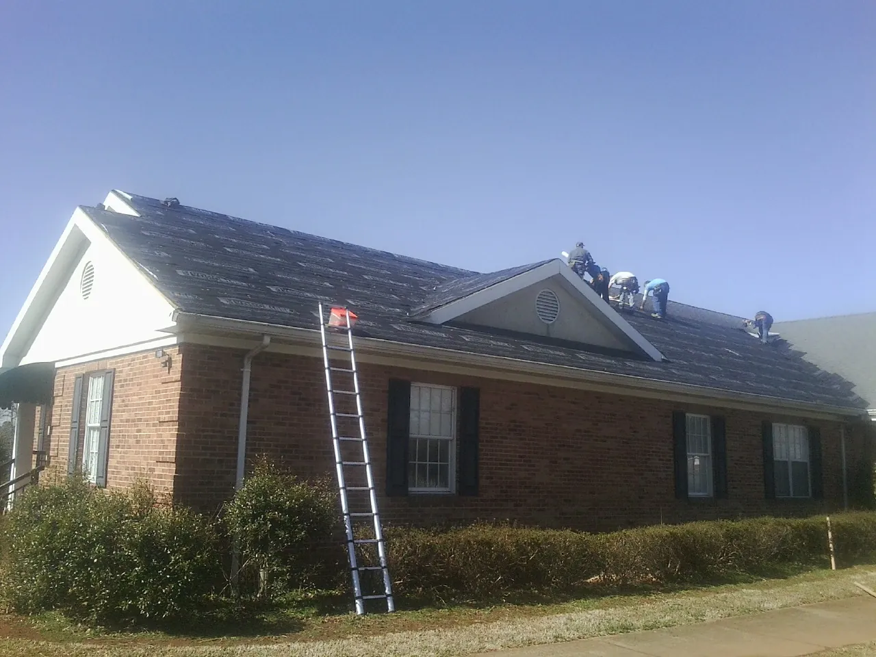 Crew tearing shingles off a brick ranch roof with a ladder set — Emergency Roof Repair work by our crew in Aripeka
