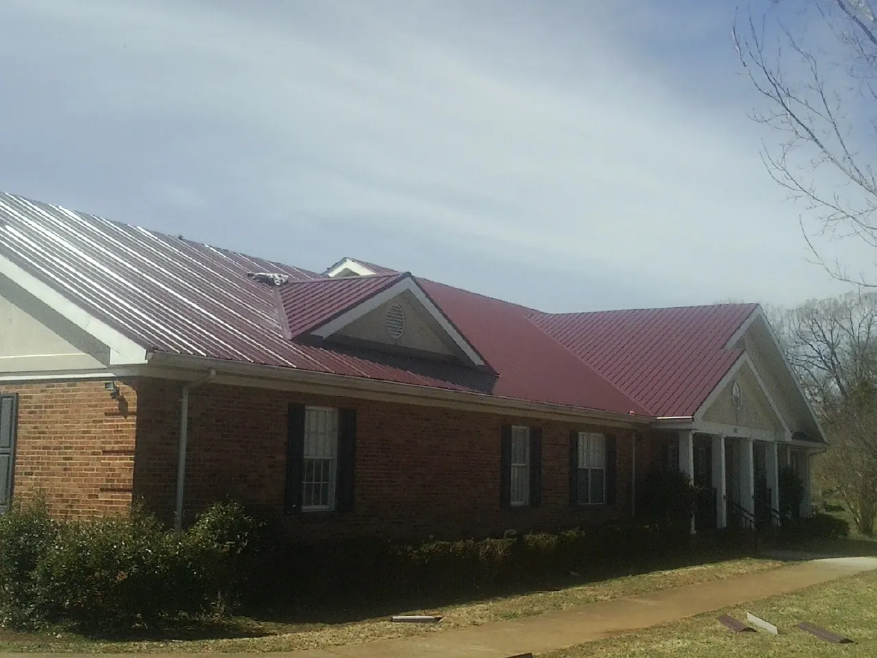 Red metal roof with gabled entries on a long brick building, from a Hail Damage Roof Repair job in Aripeka