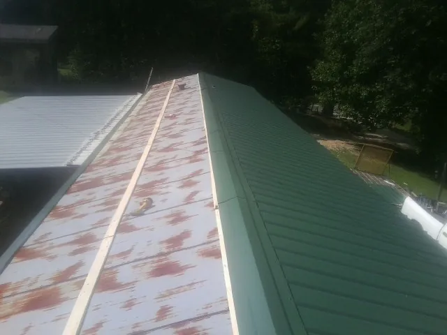Old rusted panels beside newly installed green metal roofing — Wind Damage Roof Repair by Roofing Brothers in Aripeka