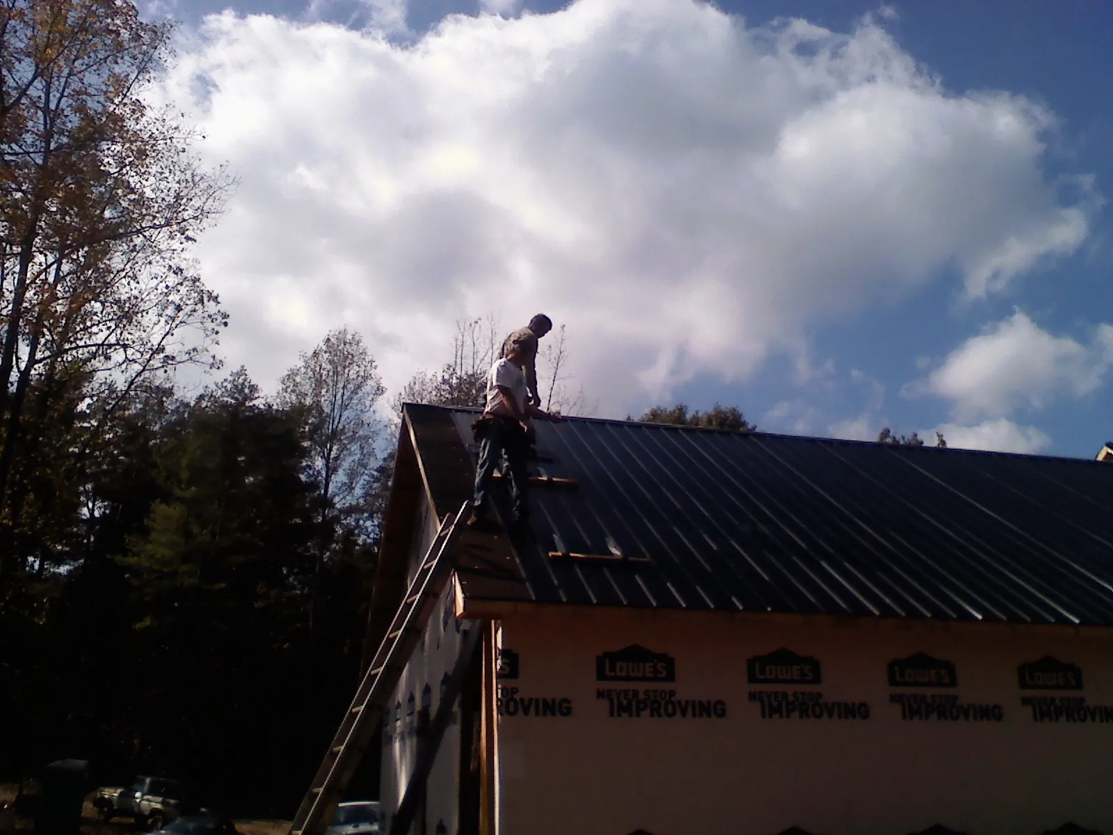 Roofer fastening dark metal panels high against a cloudy sky, from a Roof Inspection job in Aripeka