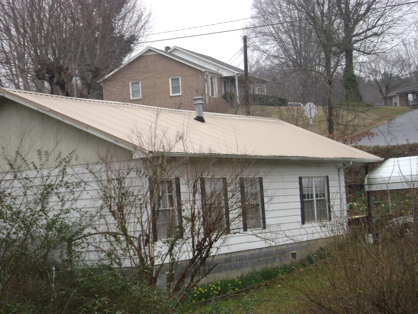 Tan metal roof on a white sided house set into a hillside — Commercial Roofing by Roofing Brothers in Aripeka